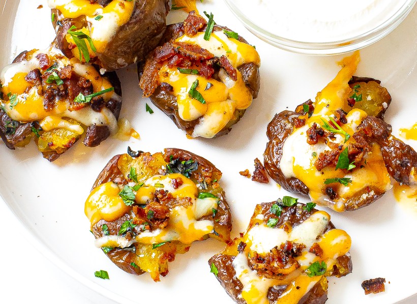 Loaded smashed potatoes with melted cheese, bacon and parsley on top.